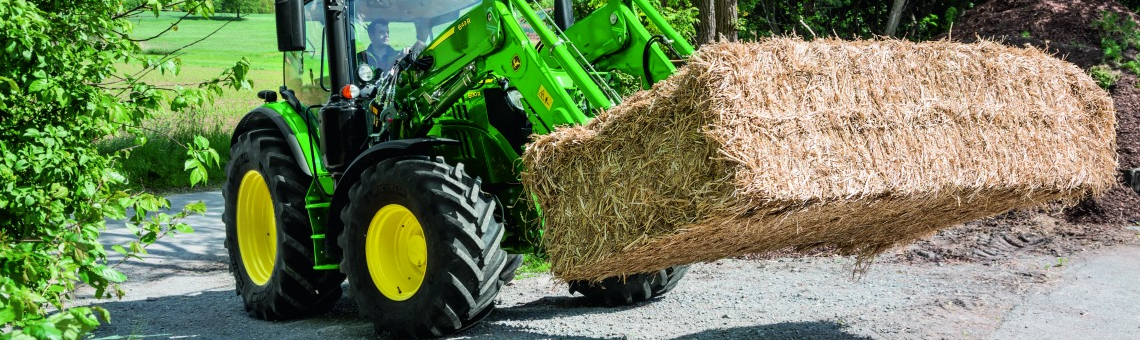 Man in a John Deere® 6R tractor carrying a bale of hay 